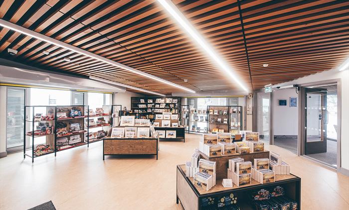 A large, brightly lit gift shop. Two display tables are in the centre of the picture with shelving units behind.